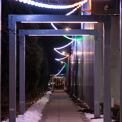 A path at night with lights strung above it. There are some arches above the path.