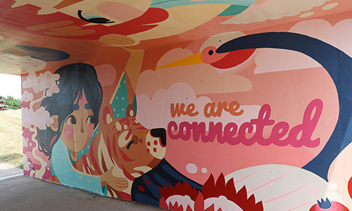 Women of Achievement Bridge Mural A painted mural under a bridge of a young girl among flowers and animals. The words "We are connected" are painted.
